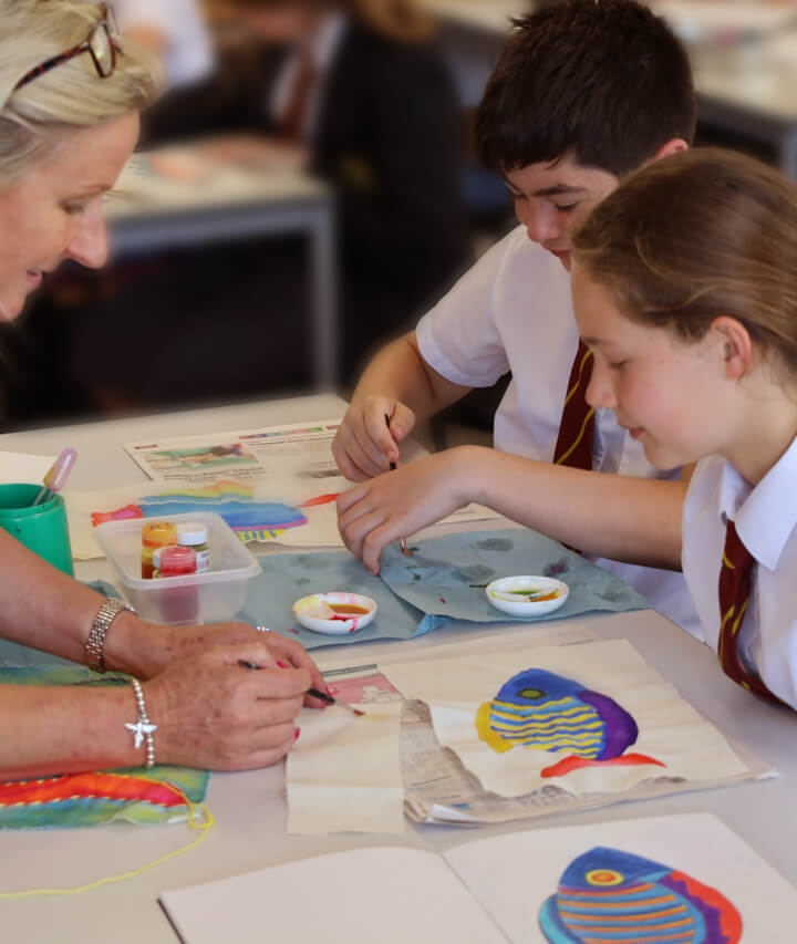 Bright art classroom with students and teacher working on colourful projects.