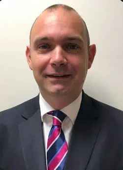 Young man in formal suit and tie at Kings School Hants classroom.