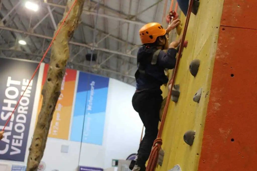 Child wearing helmet and harness enjoying indoor rock climbing experience.