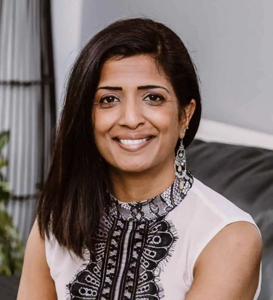 A professional woman with dark hair and earrings, smiling in an office setting.