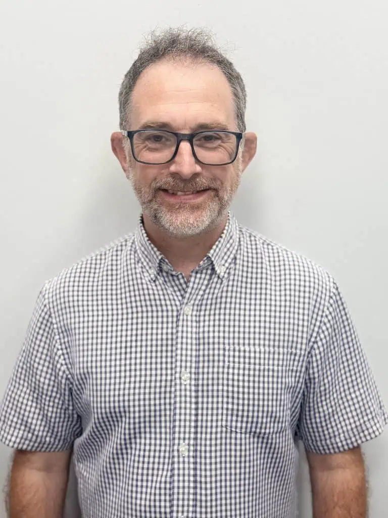 Man with glasses and checkered shirt, smiling, in a professional setting.